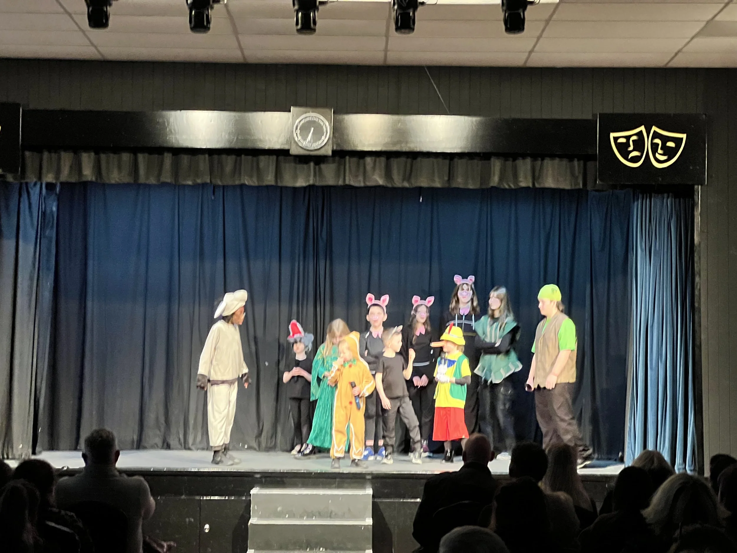 Children performing on stage wearing animal costumes, including mice, rabbits, and dogs, with an audience watching.