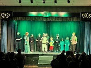 People dressed in costumes on stage during a performance, with an audience watching.