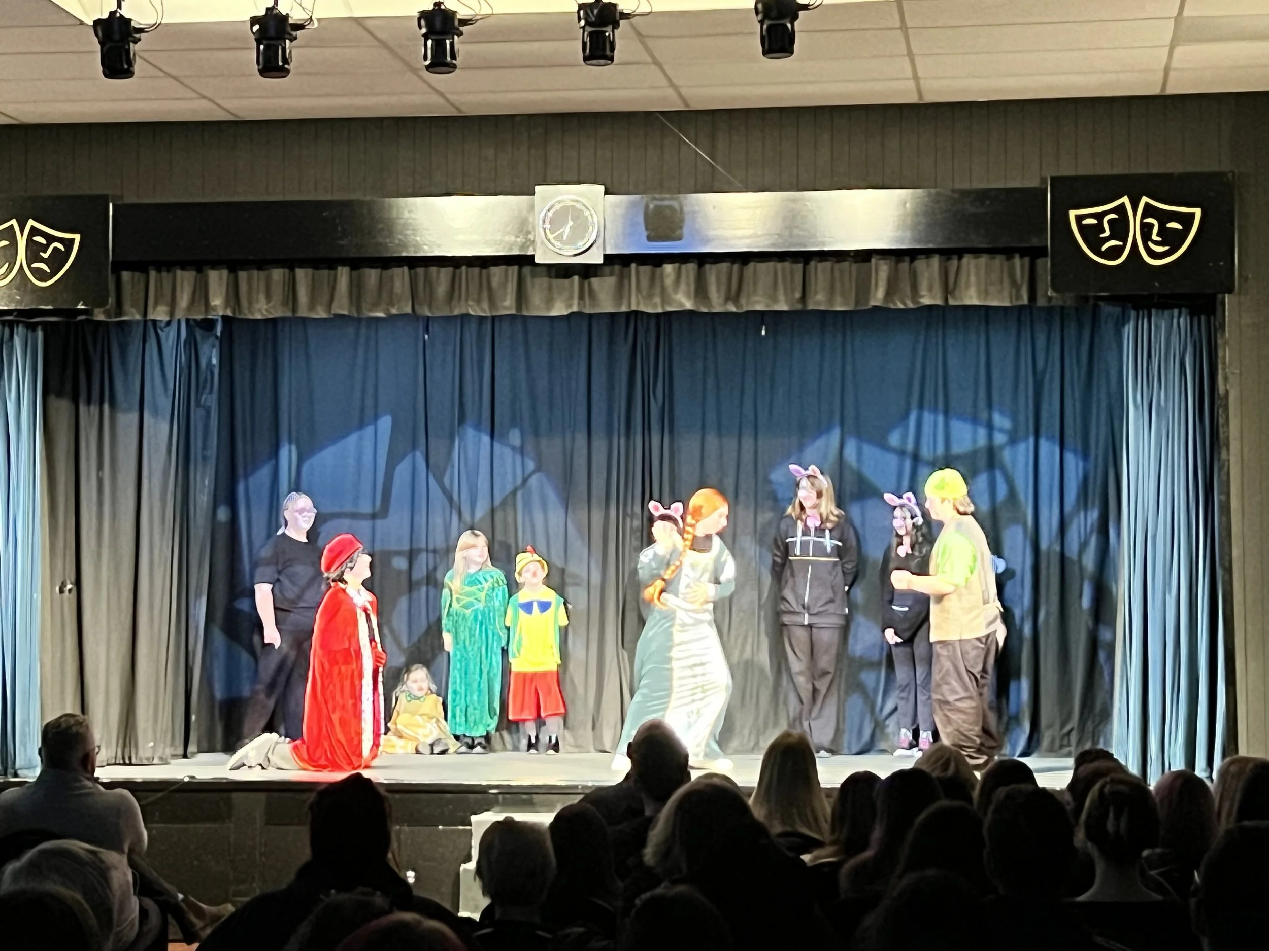 Children performing a play on stage with costumes, some wearing animal ears, in front of an audience