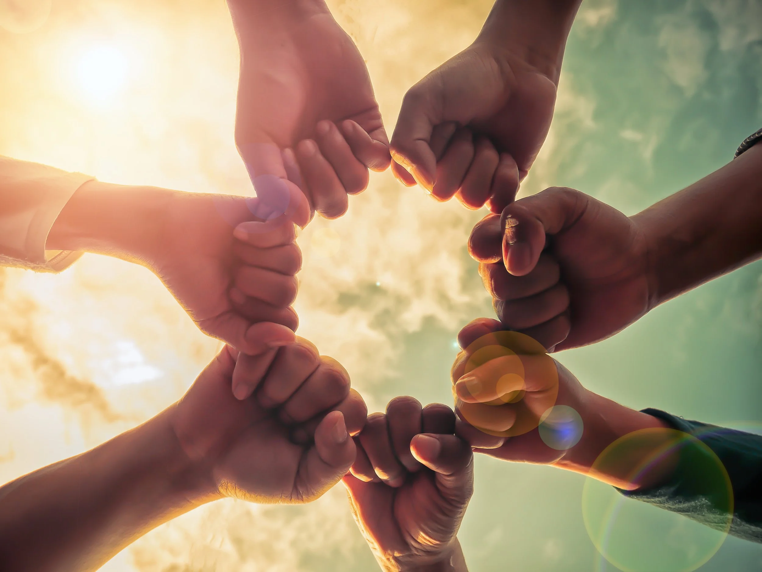 Six hands joined together in a circle against a bright sky
