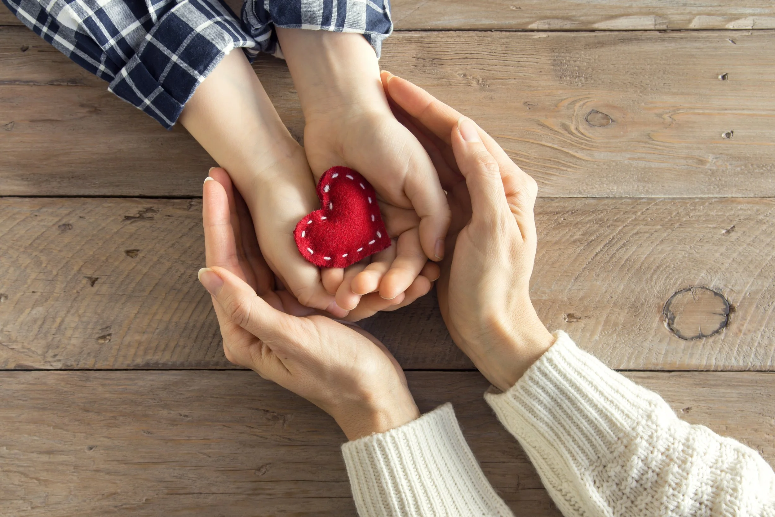 An adult's hands cupping a child's hands holding a small red fabric heart