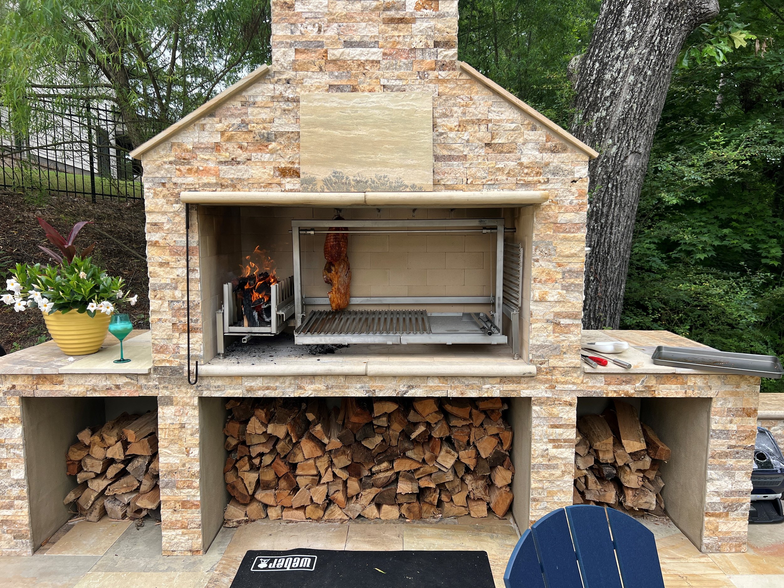 Argentinian Grill Insert in a wooded setting grilling prepared meats and vegetables.