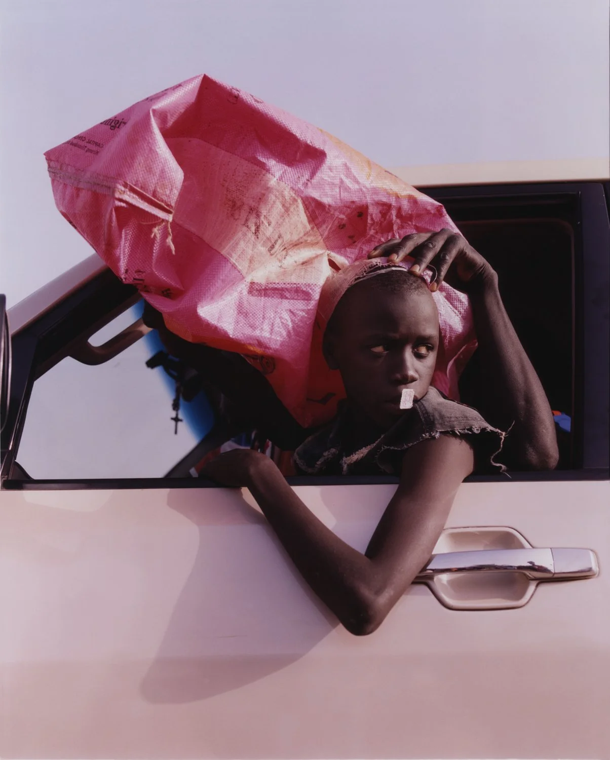 Image of a child with one arm out the window of a pink car, with a stamp stuck to their lips.