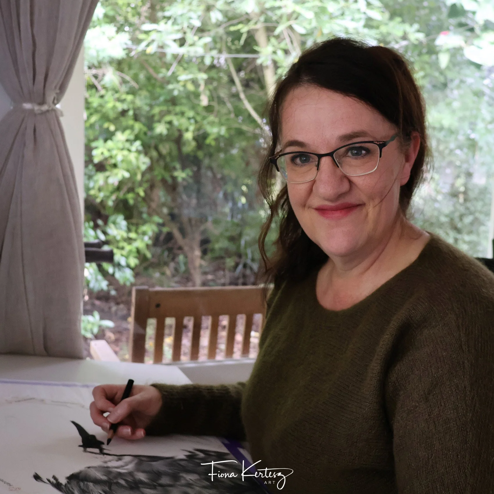 photo of Fiona Kertesz smiling at the camera while working on her charcoal drawing.