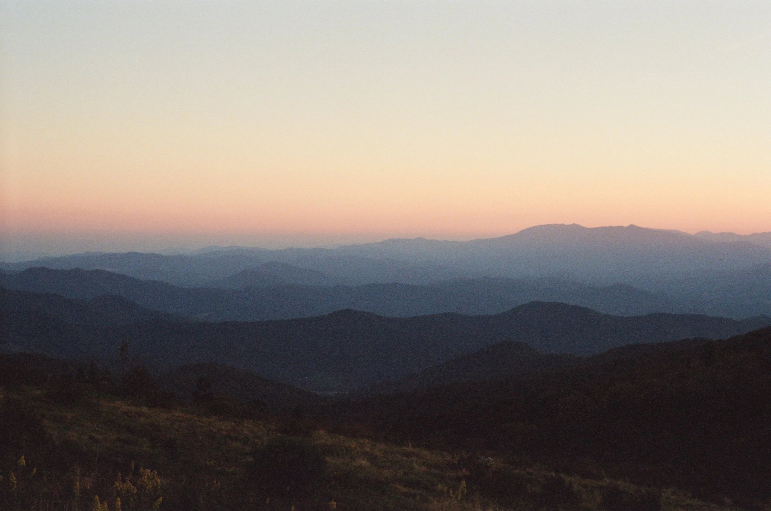 A landscape of distant mountains and hills at dusk with a colorful sunset sky.