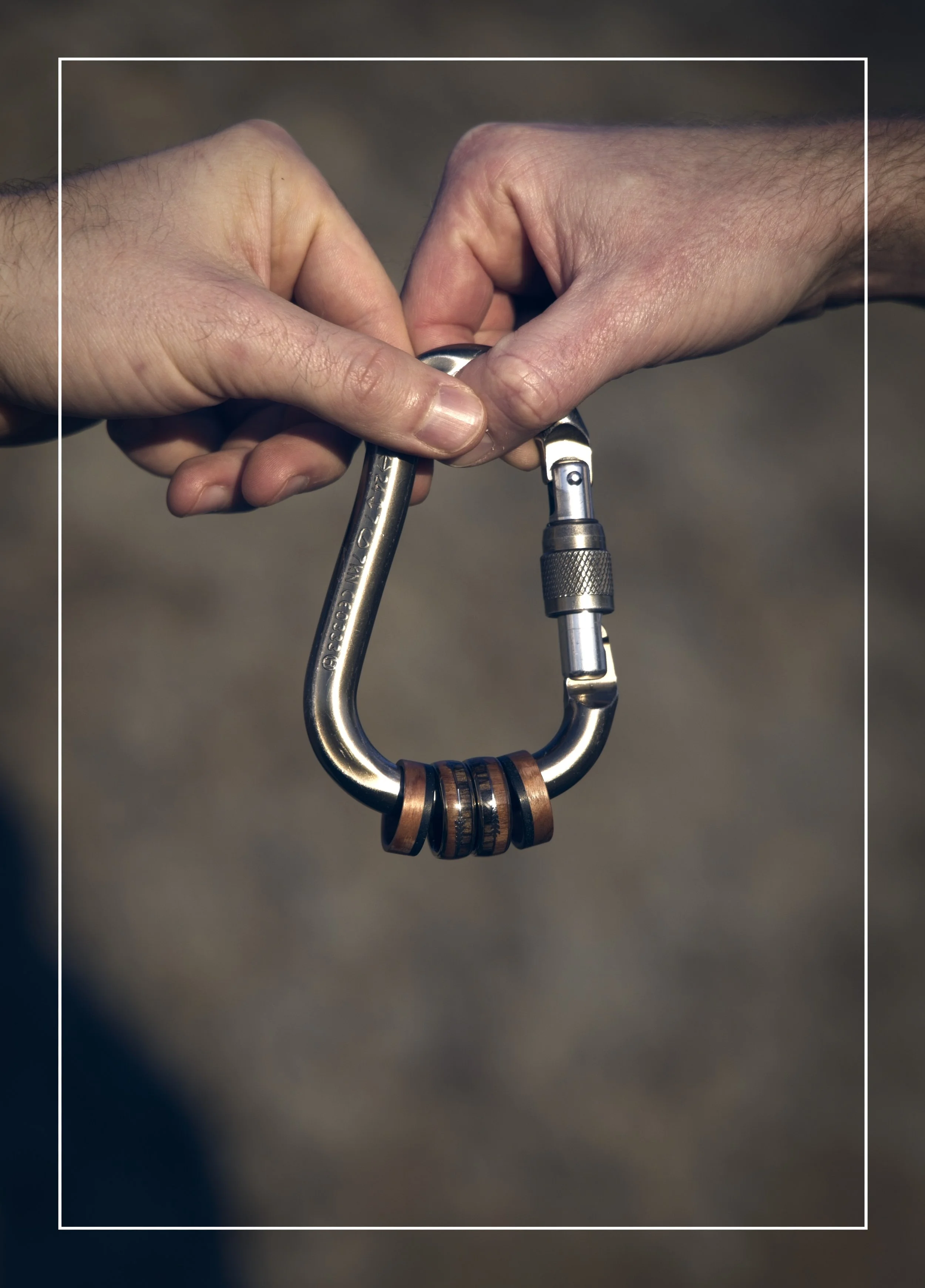 Two hands connecting a carabiner with rings on it, with a blurred background.