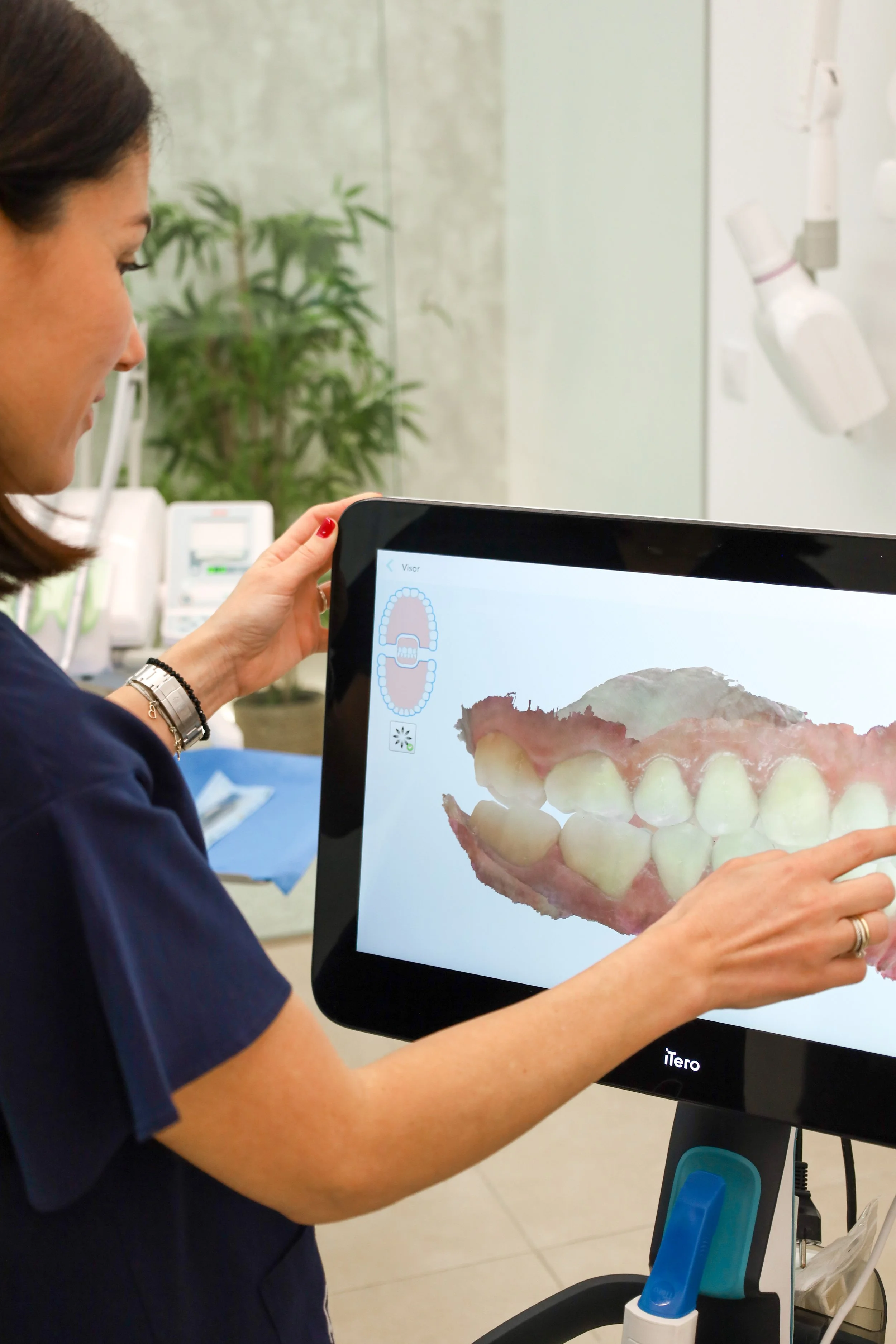 Persona en una clínica dental utilizando una pantalla interactiva que muestra una imagen digital de dientes y encías.