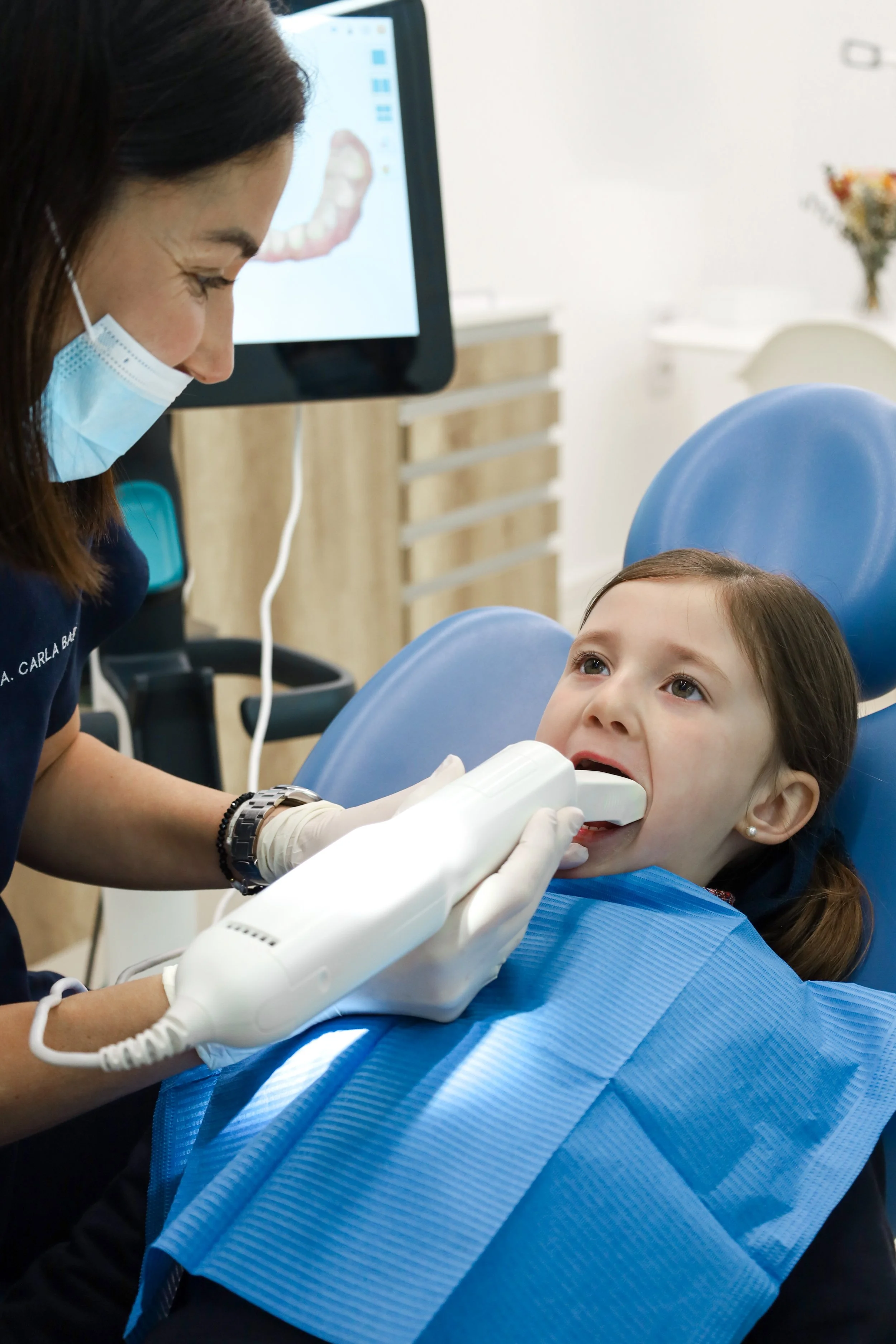 Fillette dans un cabinet dentaire avec un dentiste utilisant un scanner intra-oral pour vérifier ses dents.