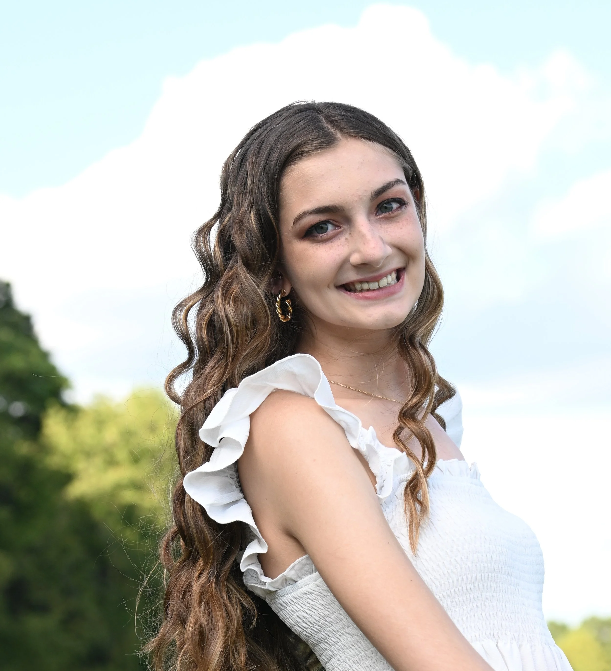 A volcanic landscape with colorful rocky terrain, steam rising from the ground, patches of snow, and a glacier in the background under a cloudy sky.