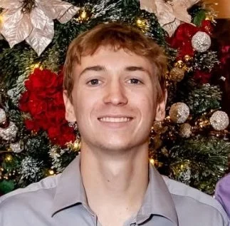A rugged landscape with colorful volcanic rocks, steam vents, and patches of snow on a mountainous terrain under a cloudy sky.