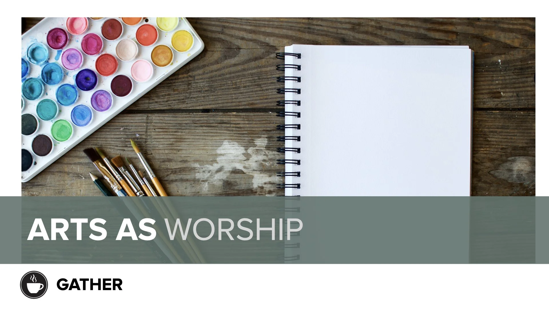 Watercolor paint palette, paintbrushes, and a blank spiral notebook on a wooden table, with a banner reading "Arts as Worship."