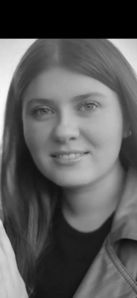 A rugged volcanic landscape with brownish-yellow rocks, patches of snow, and a glacier in the background under a cloudy sky.