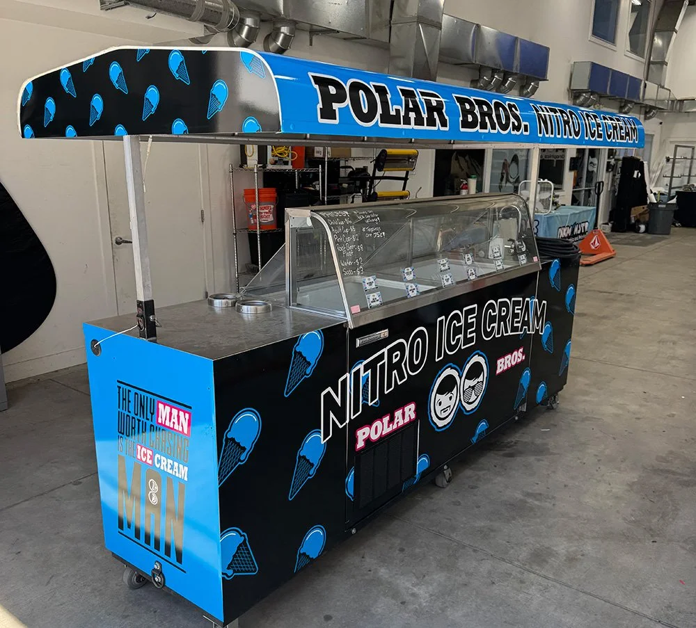 A mobile ice cream cart with branding for Polar Bros Nitro Ice Cream. The cart has a blue and black color scheme with ice cream cone graphics. 
