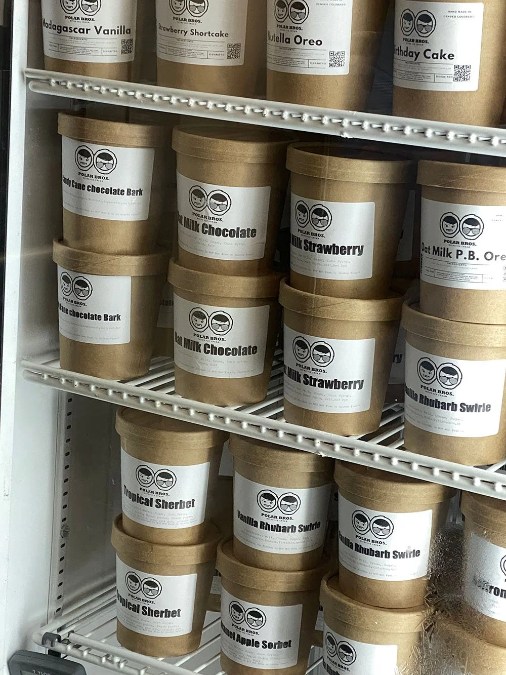 Polar Bros Nitro Ice Cream pints labeled with flavors such as Madagascar Vanilla, Strawberry Shortcake, Nutella Oreo, and others, arranged on shelves in a refrigerator.