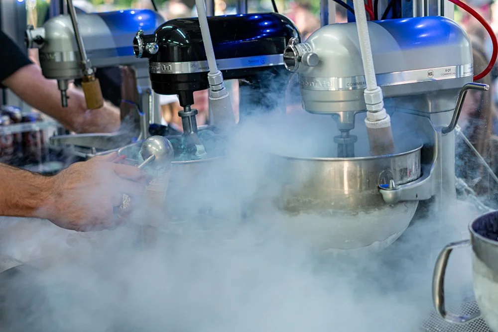 Two people operating a large commercial Liquid Nitrogen ice cream machine with vapor around it.