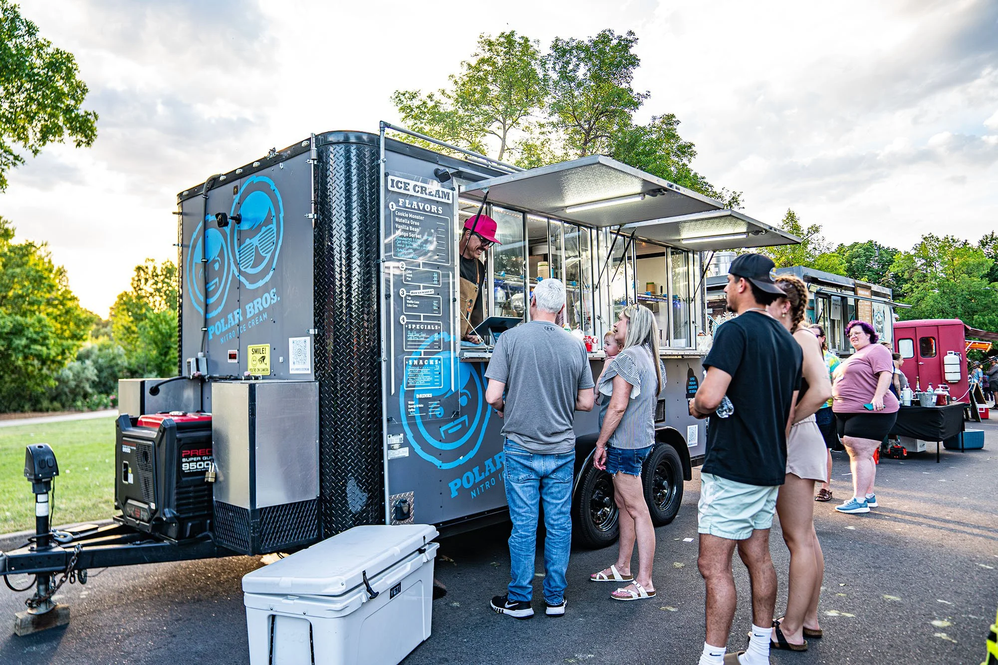 People standing in line at a Polar Brod Nitro ice cream truck in a park during the day.