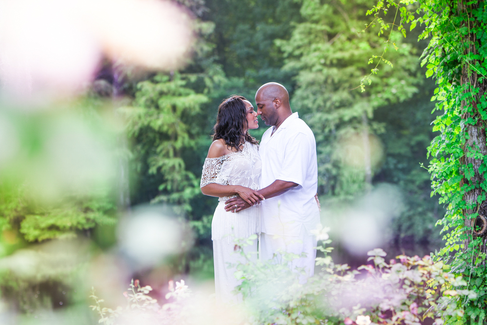  Husband and wife embrace in a natural setting surrounded by greenery. 