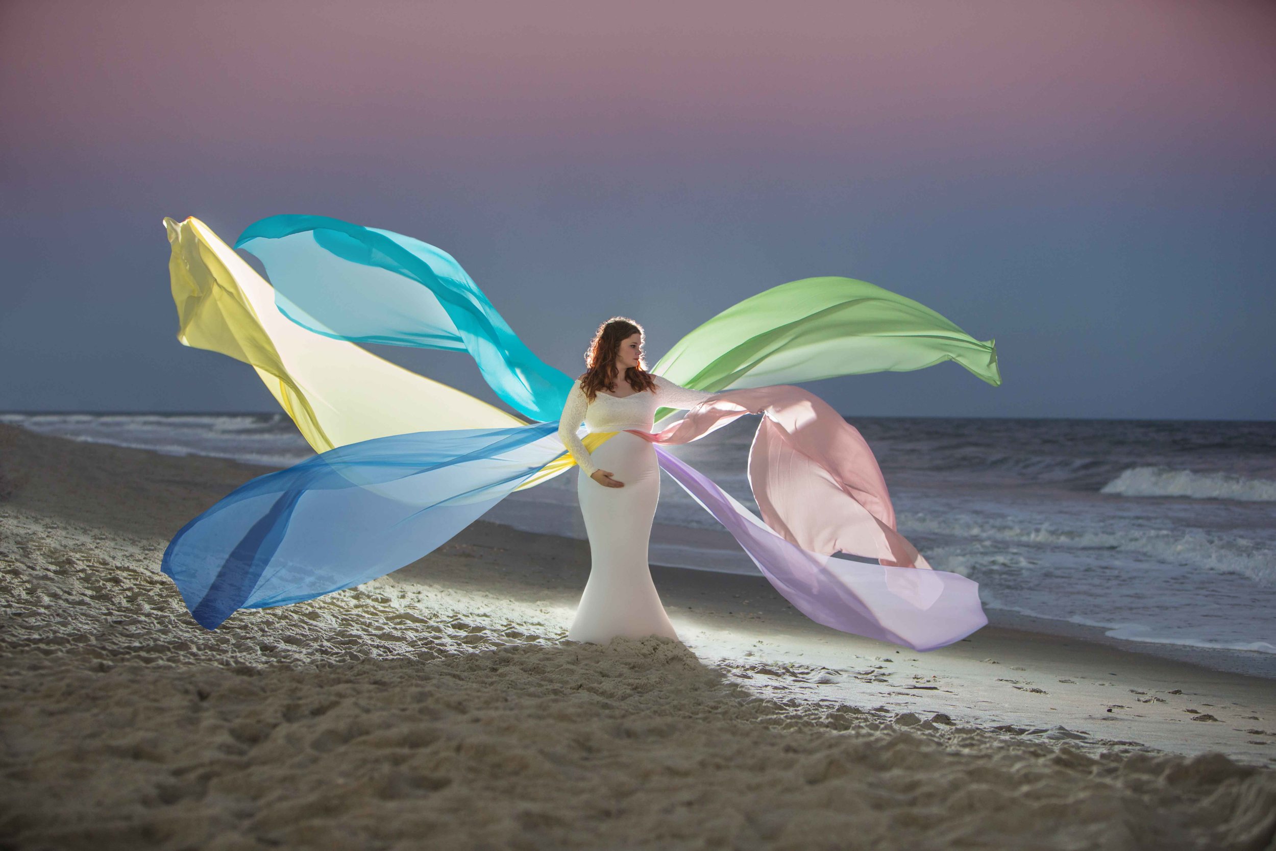  Maternity session on the beach with colorful ribbons flowing from dress. 