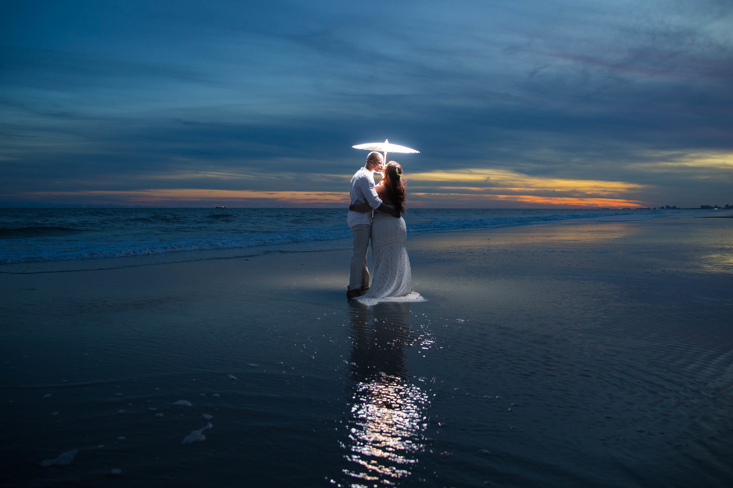  Couple kisses on a beach during sunset with an illuminated umbrella. 