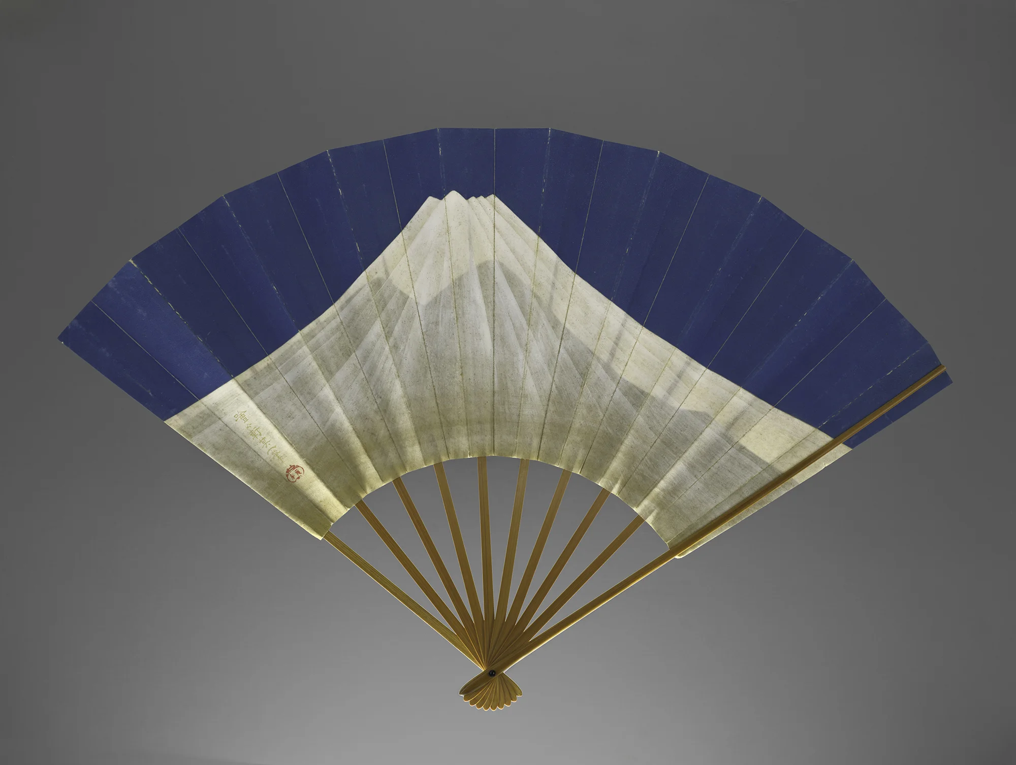 Traditional Japanese folding fan with a painting of Mount Fuji against a gray background.
