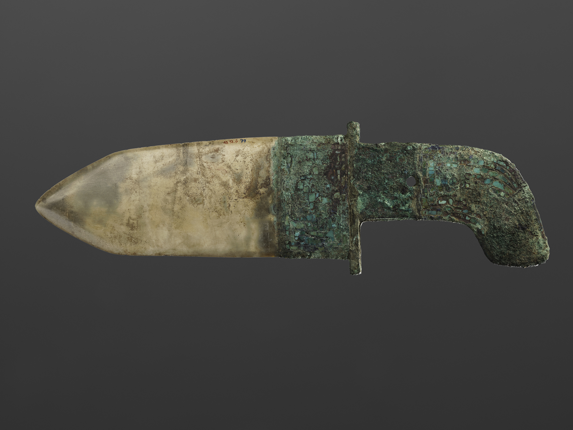 A ceremonial dagger with a curved blade and a decorated hilt featuring turquoise inlays, showing signs of age and corrosion, against a grey background.