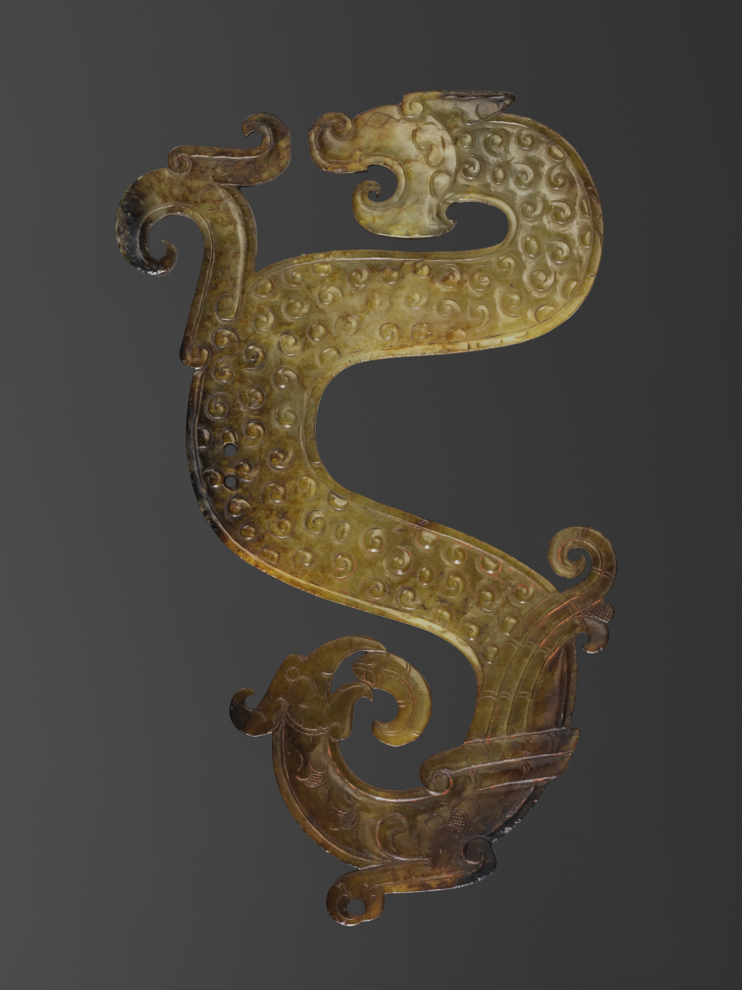 Carved jade pendant with intertwined dragon design on a gray background.