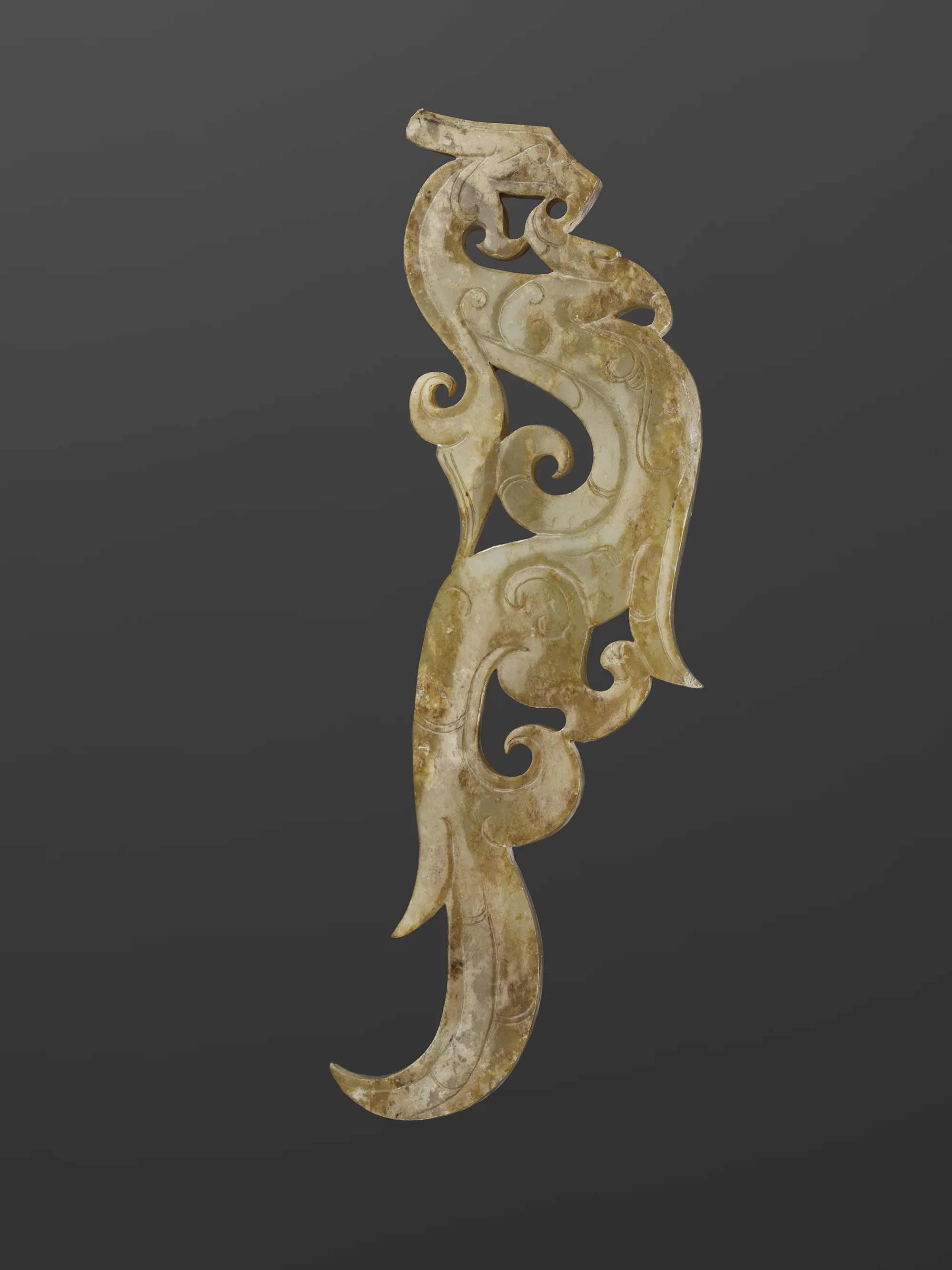 An intricately carved, decorative jade pendant featuring a stylized animal, possibly a dragon or mythical creature, with swirling patterns on a gray background.
