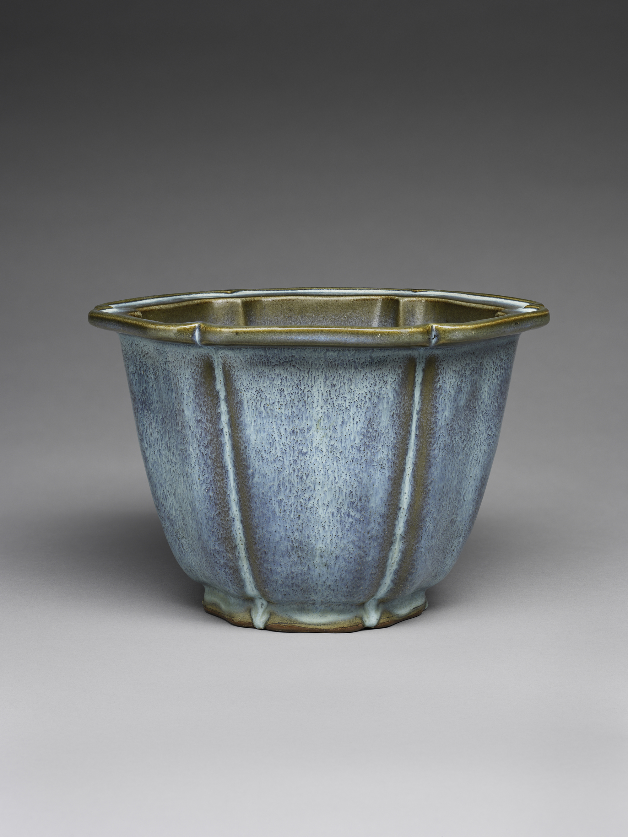 Ceramic blue-green glazed bowl with vertical ridges and irregular rim, seen against a gray background.