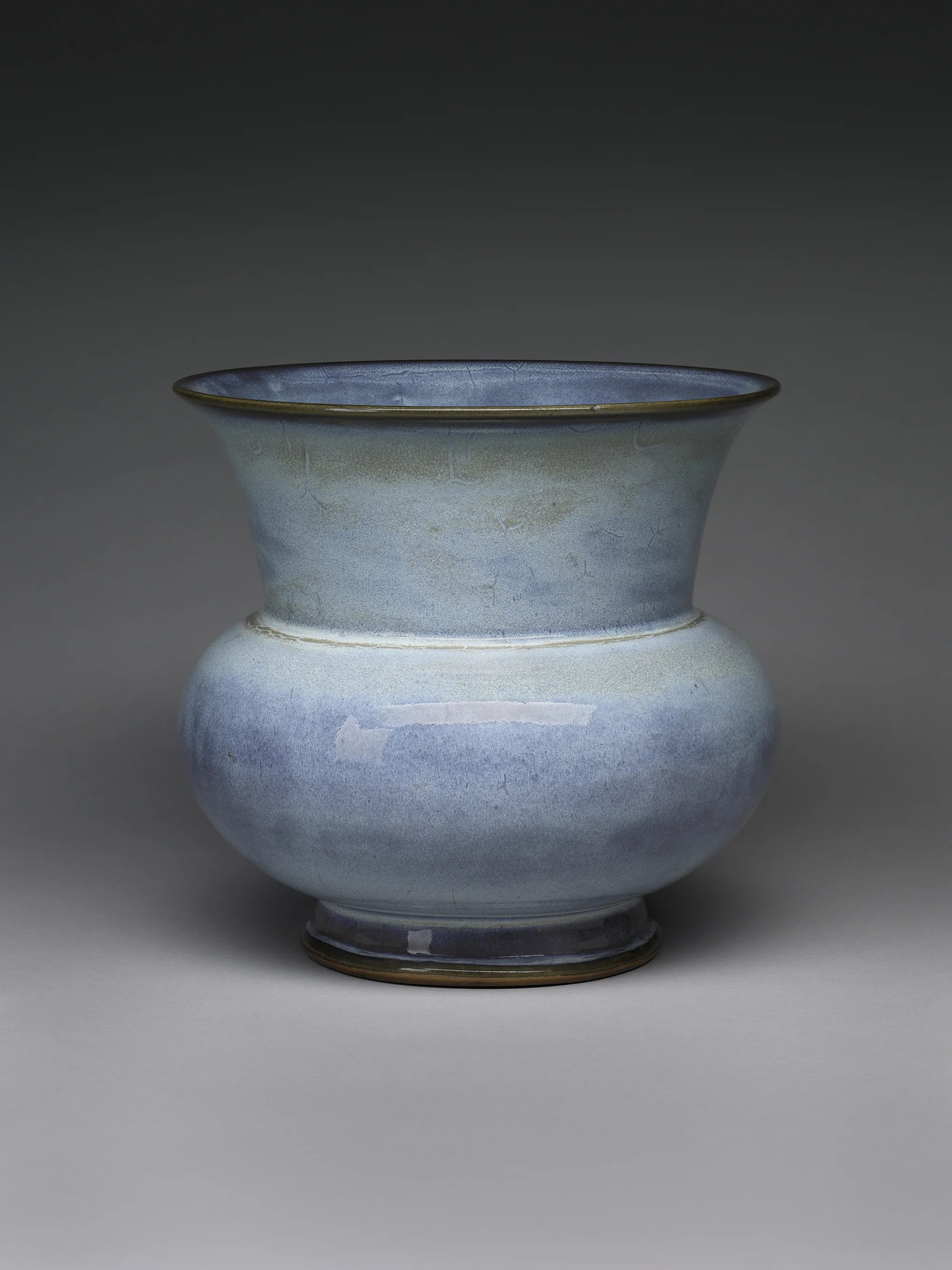 A blue glazed ceramic vase with a rounded body, a narrow neck, and a flared rim, set against a plain gray background.