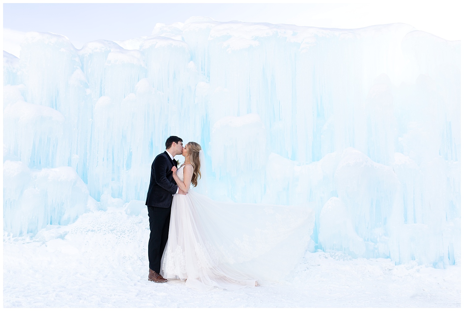 a bride and groom kiss while the bride’s dress is flying in the wind at the Dillon Ice Castles