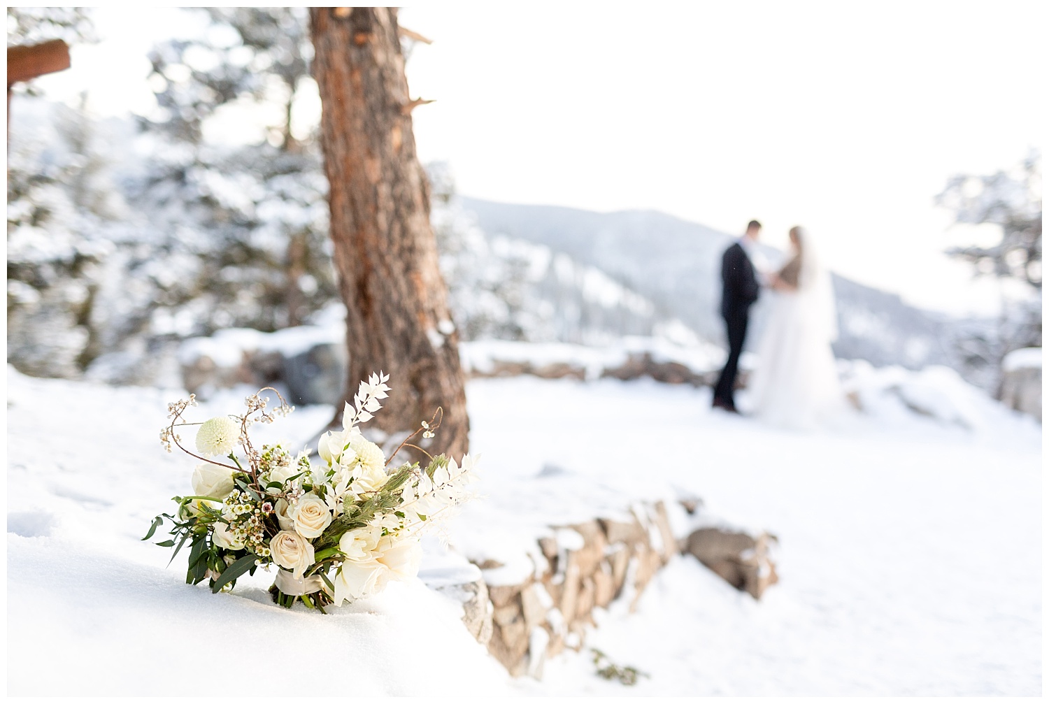 a bouquet sits in the snow with a bride and groom showing in the background