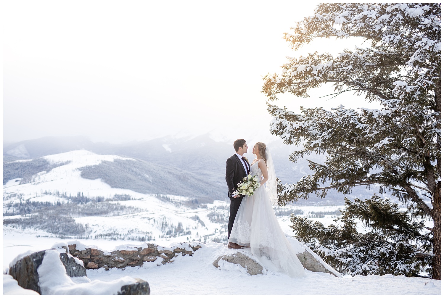 A bride and groom stand on the side of a mountain at Sapphire Point Overlook in winter