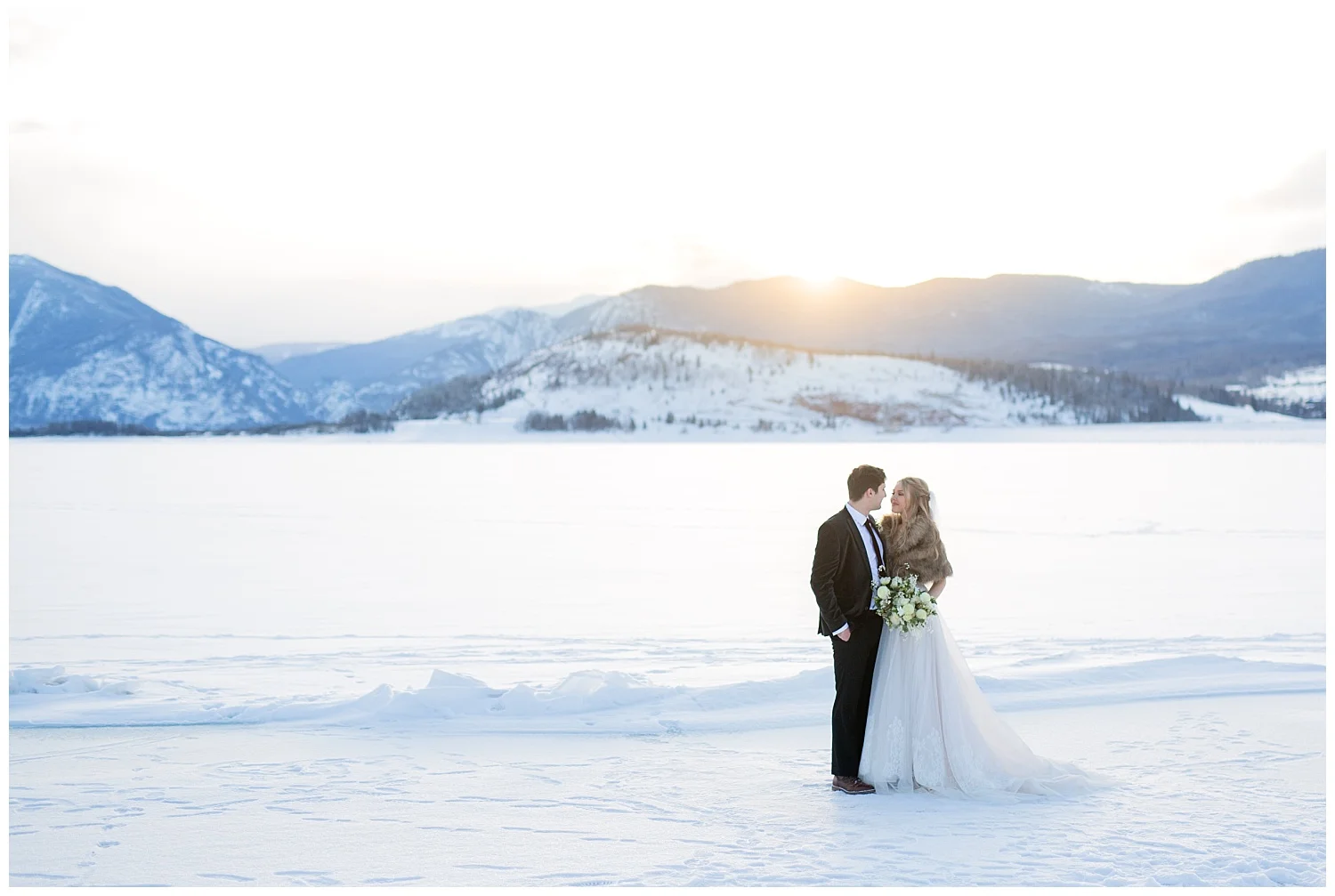 A bride and groom on a frozen lake while the sun is setting behind them