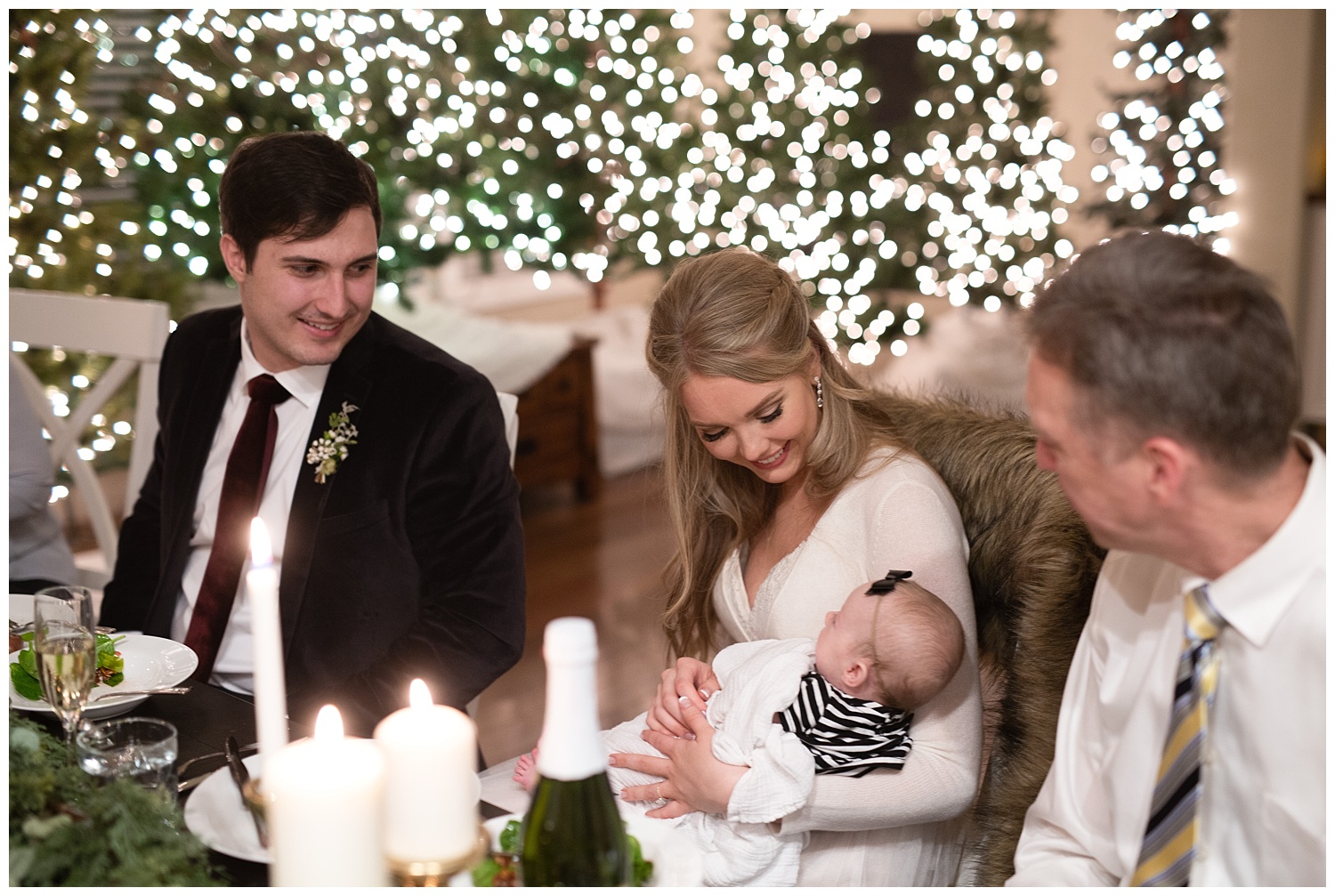 A bride and groom holding a baby while smiling at it