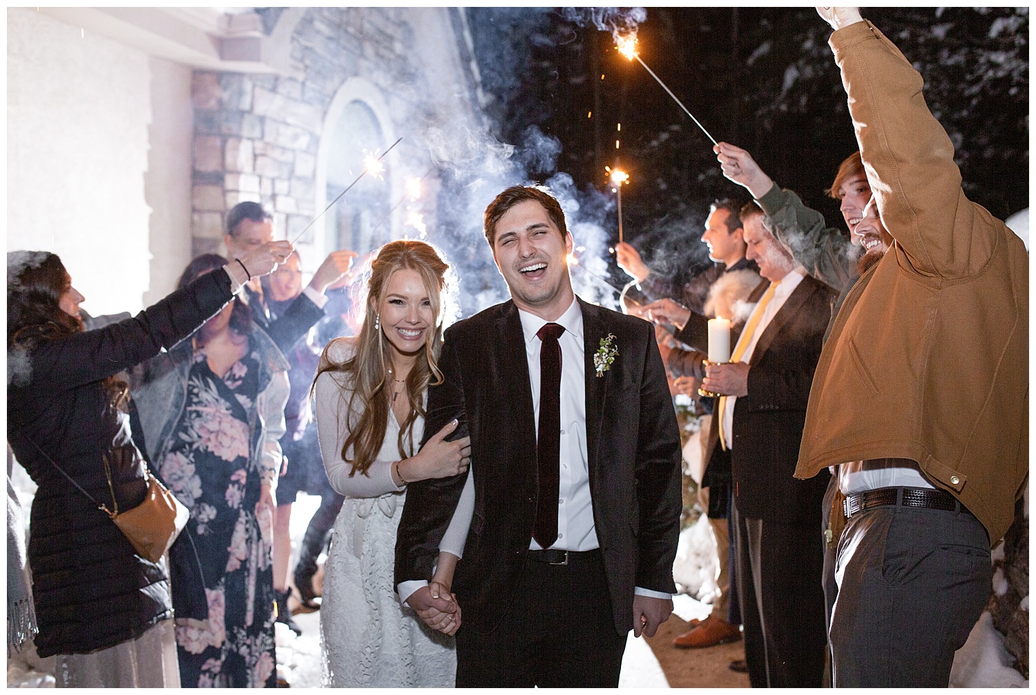 The groom laughs as the smoke from their sparkler exit lights up behind them