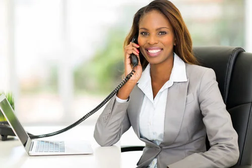 Image description: Business person holding a phone conversation at their office desk while smiling.