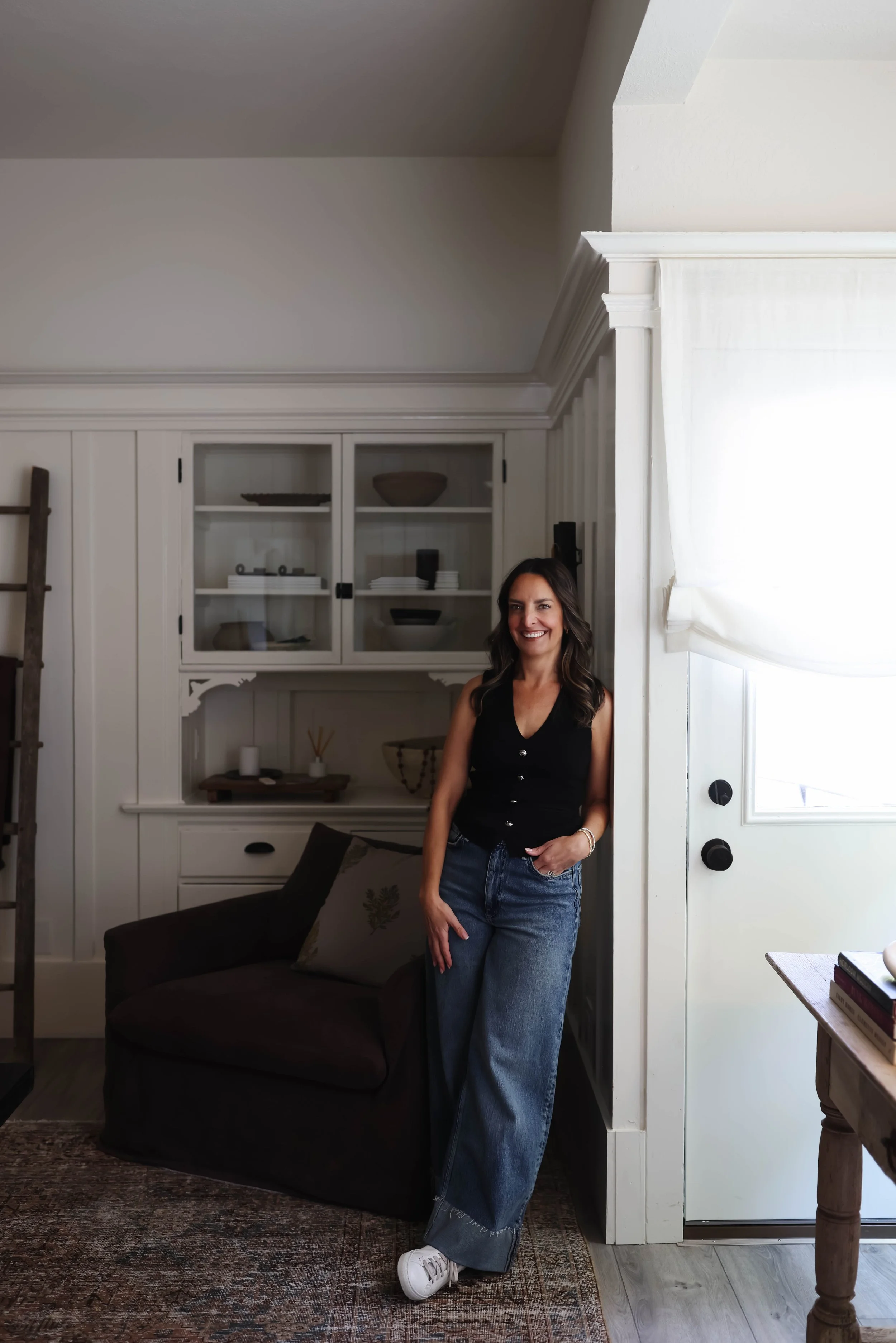 Interior designer wearing a black top and jeans leaning against a white wall