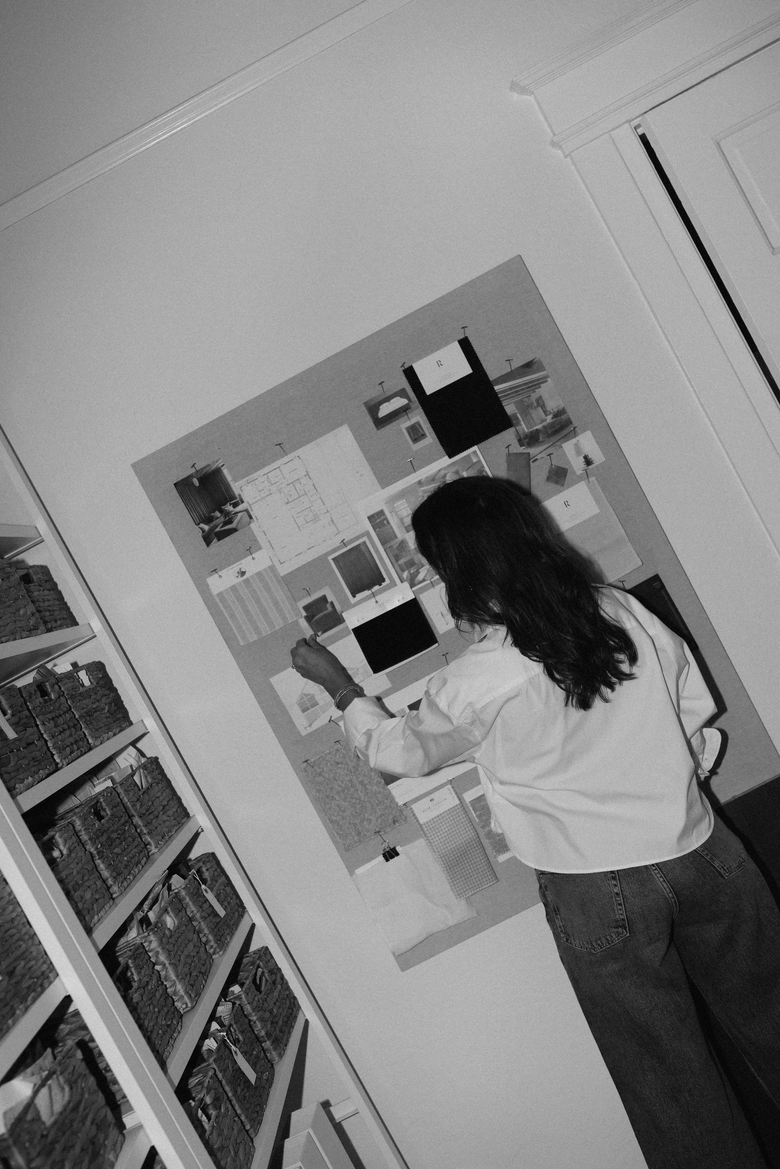  Black and white photo of Fletcher Rhodes interior designer pining inspiration images on a pin board. 