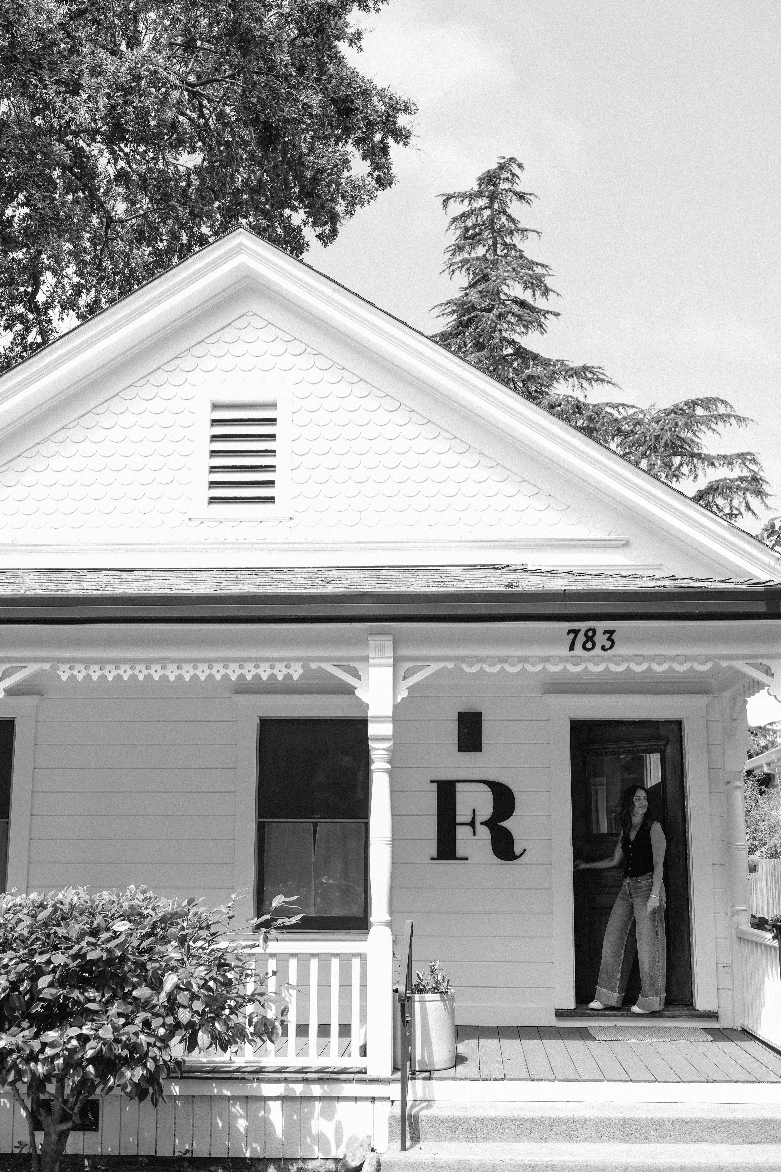  Interior designer Emily Mughannam of Fletcher Rhodes standing in the doorway of her design studio. Black and white photo. 