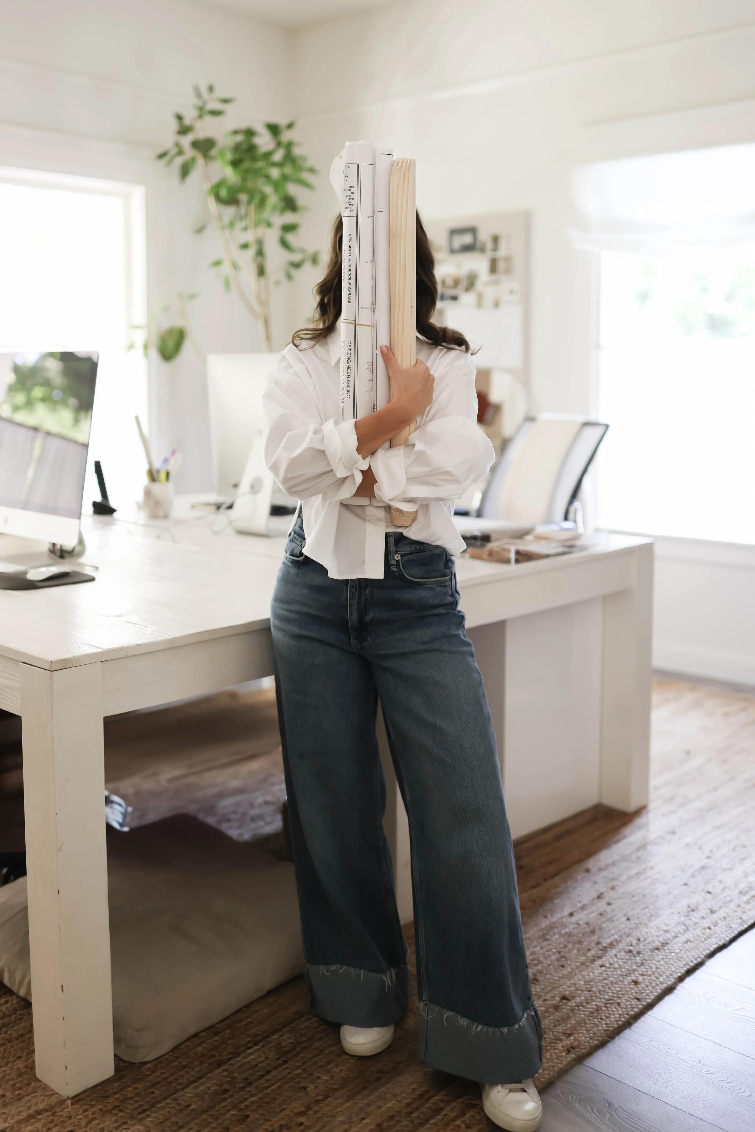 Interior designer standing in her studio, holding architecture plans in front of her face.