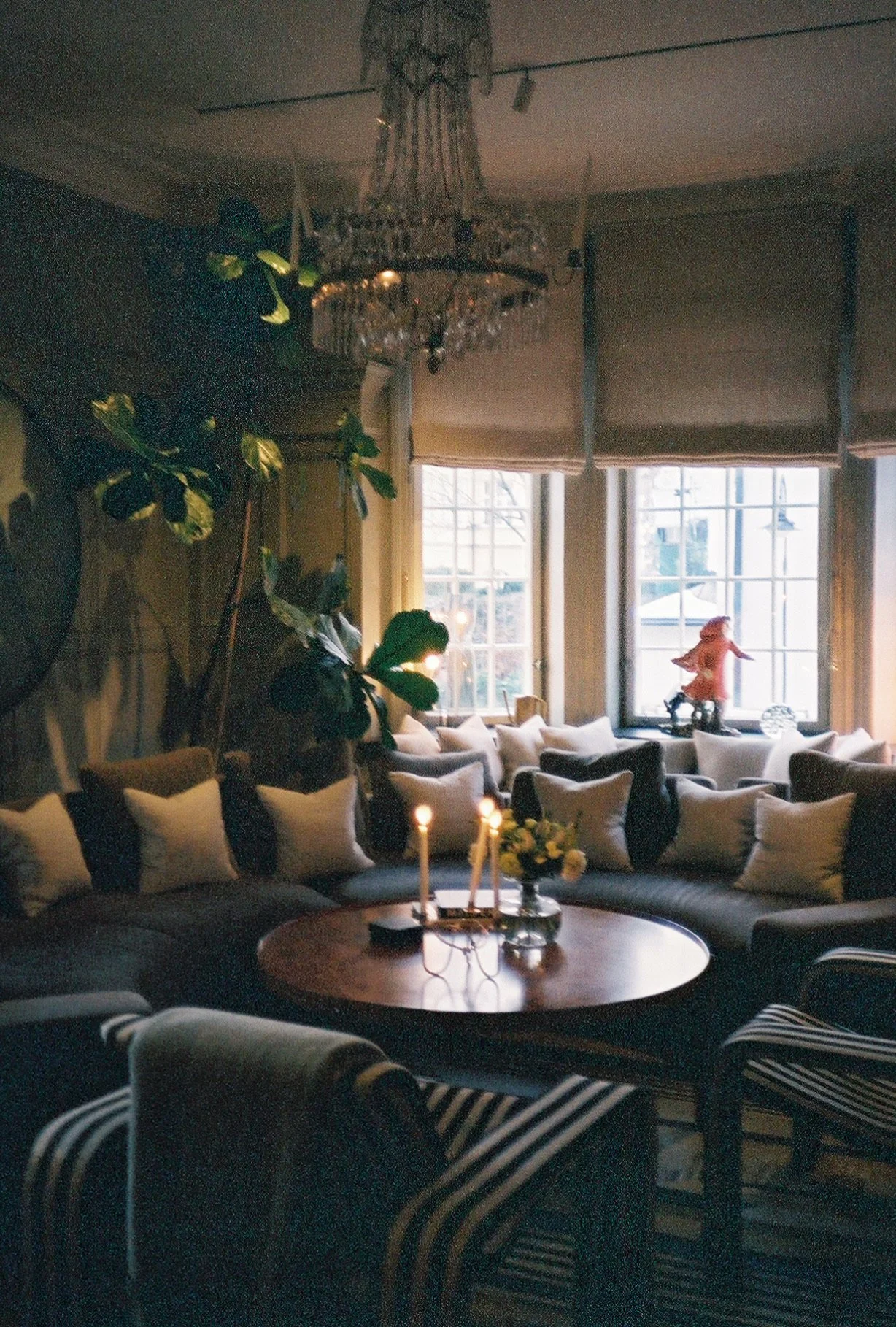 Interior of hotel at Ett Hem in Sweden. Round couch with white pillows, a large green plant in the background and large windows.