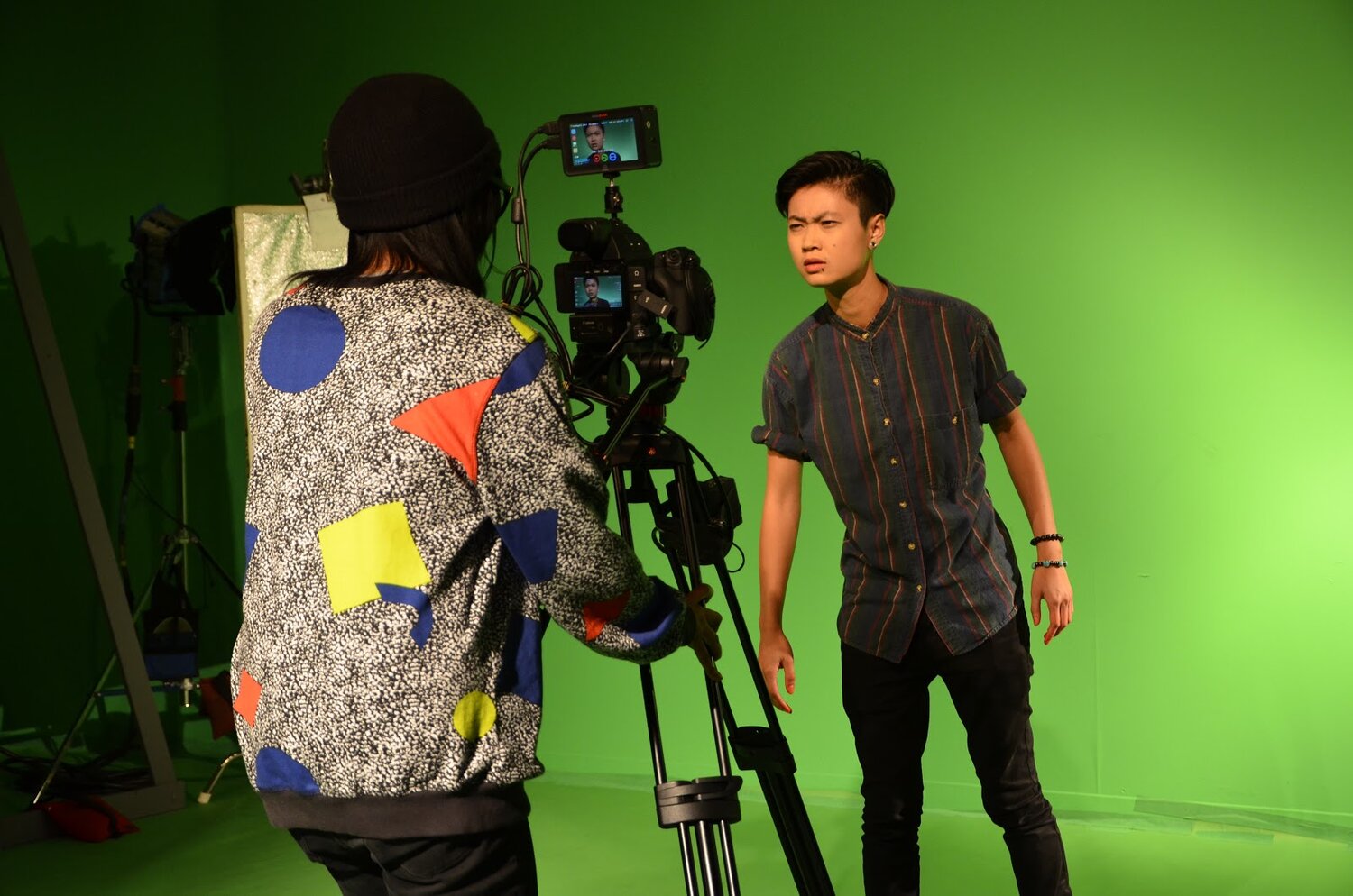  Actor Ck is standing in front of a green screen, looking into a camera, which is operated by Melinda James. 