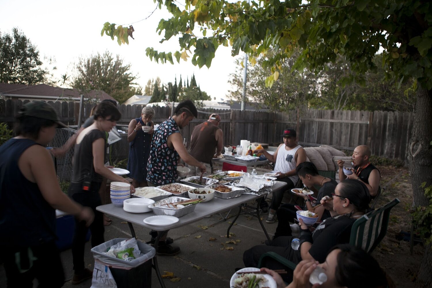  A crew of people are eating in a large backyard. 