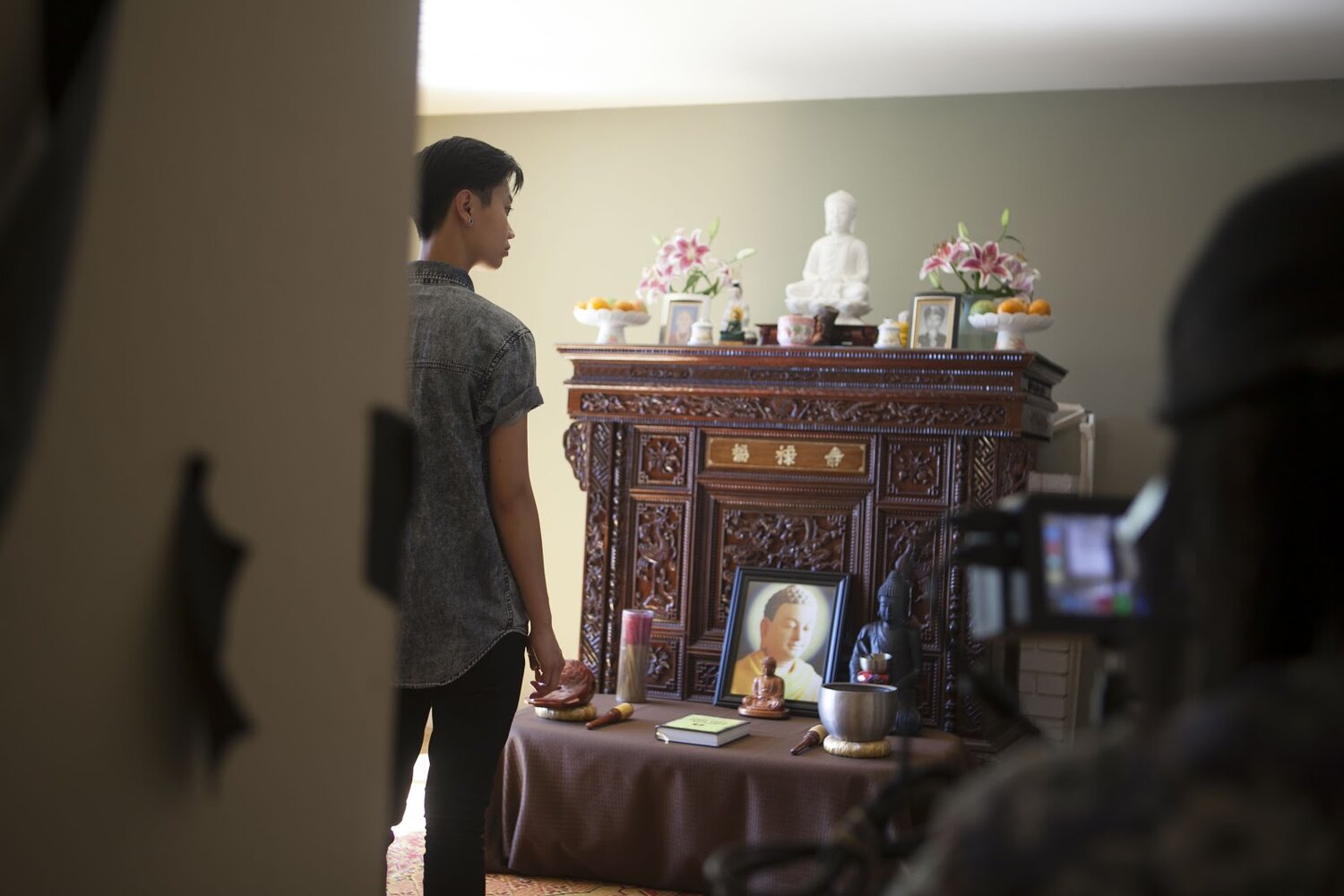  Actor Ck Ong stands in front of an altar adorned with Buddhist photos, statues, incense, and bells. 