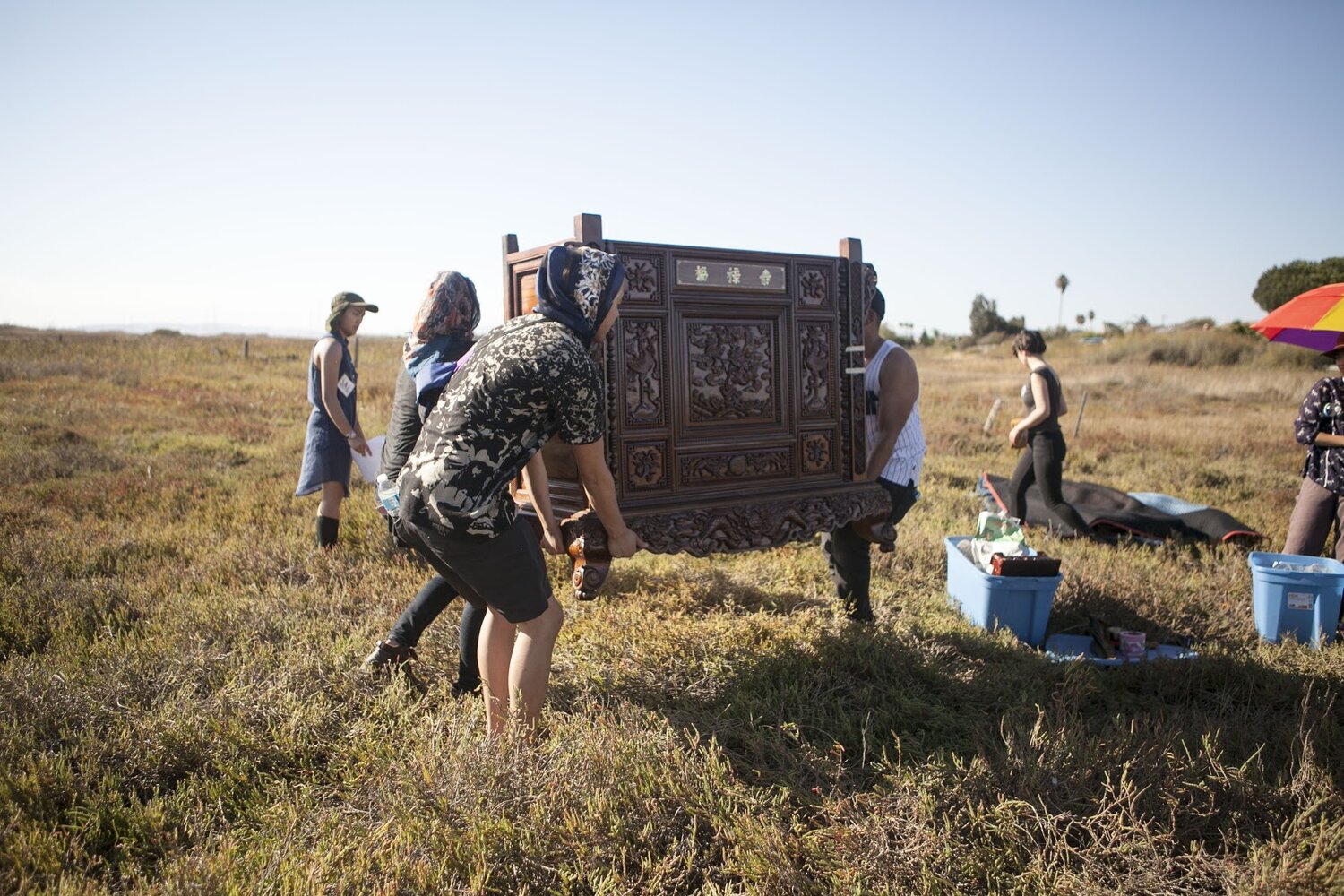  A crew of three people are hauling a 150-lb altar over an open area of dry, grass fields. 