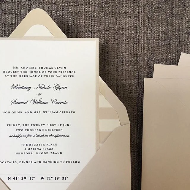 Showing off a close up of  Sam and Brit&rsquo;s custom designed wedding invitations with coordinating envelopes and cream and white striped envelope liners.