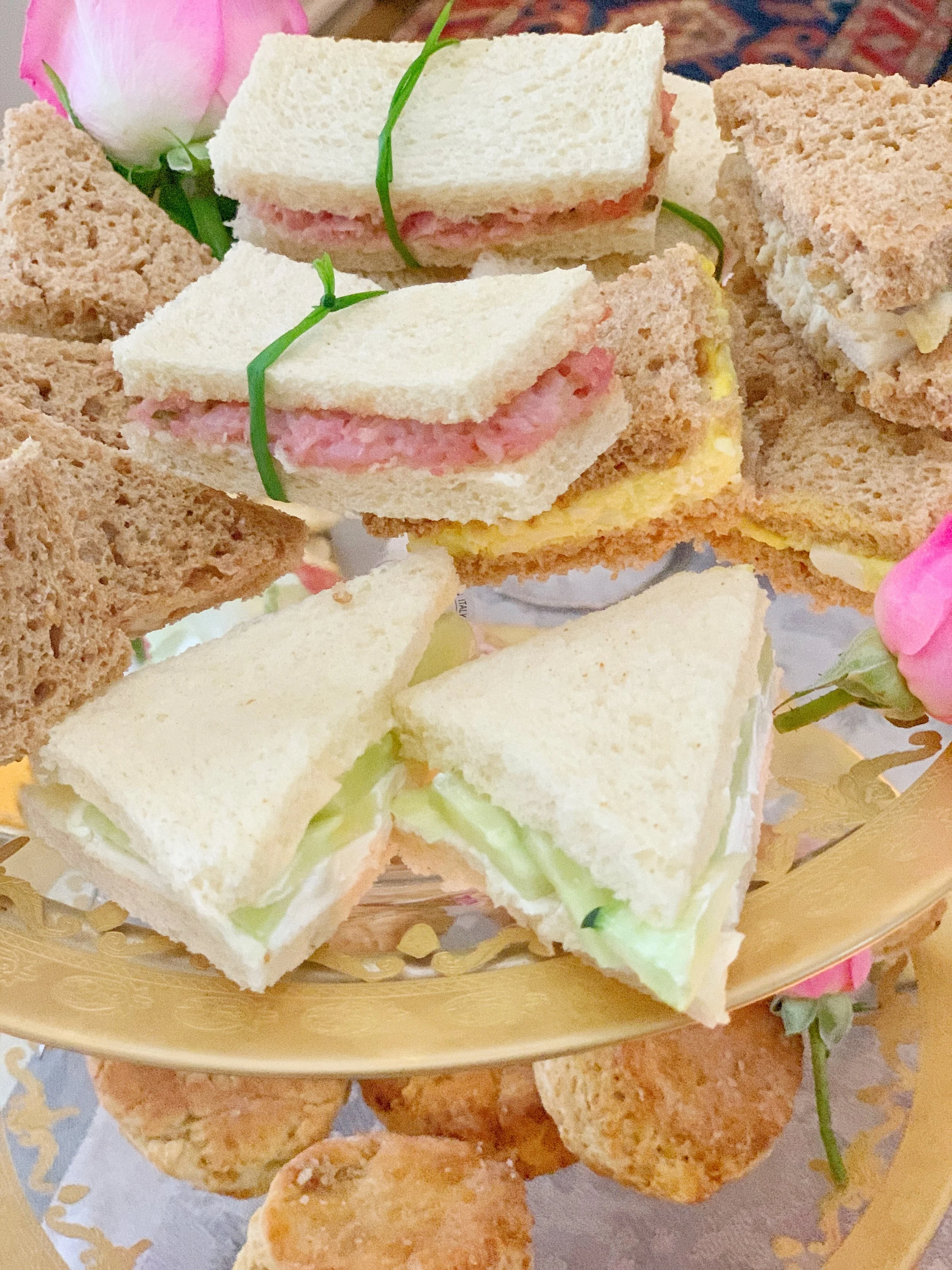 Selection of finger sandwiches and scones for an Easter high tea, including egg and dill, ham and pickle, chicken salad, and cucumber with cream cheese.