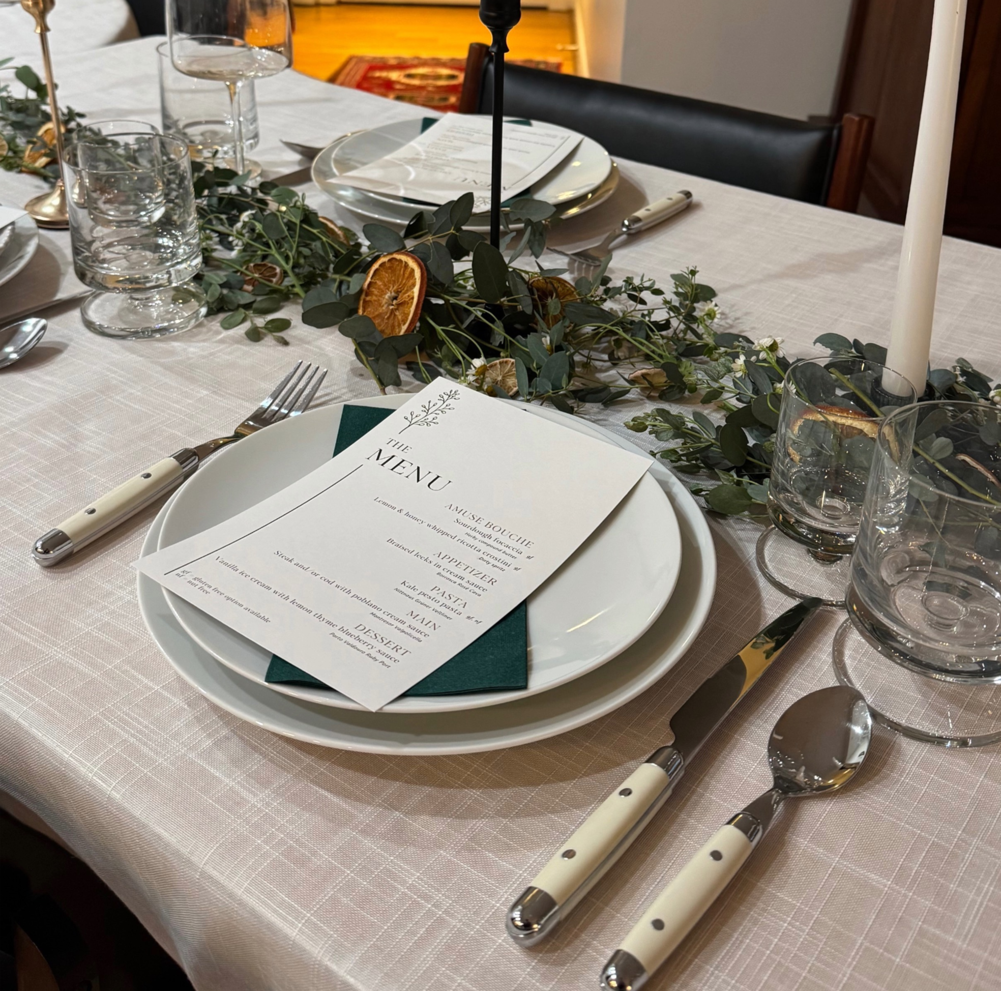 White mid century china place setting with modern French bistro flatware and printed menu on linen tablecloth.