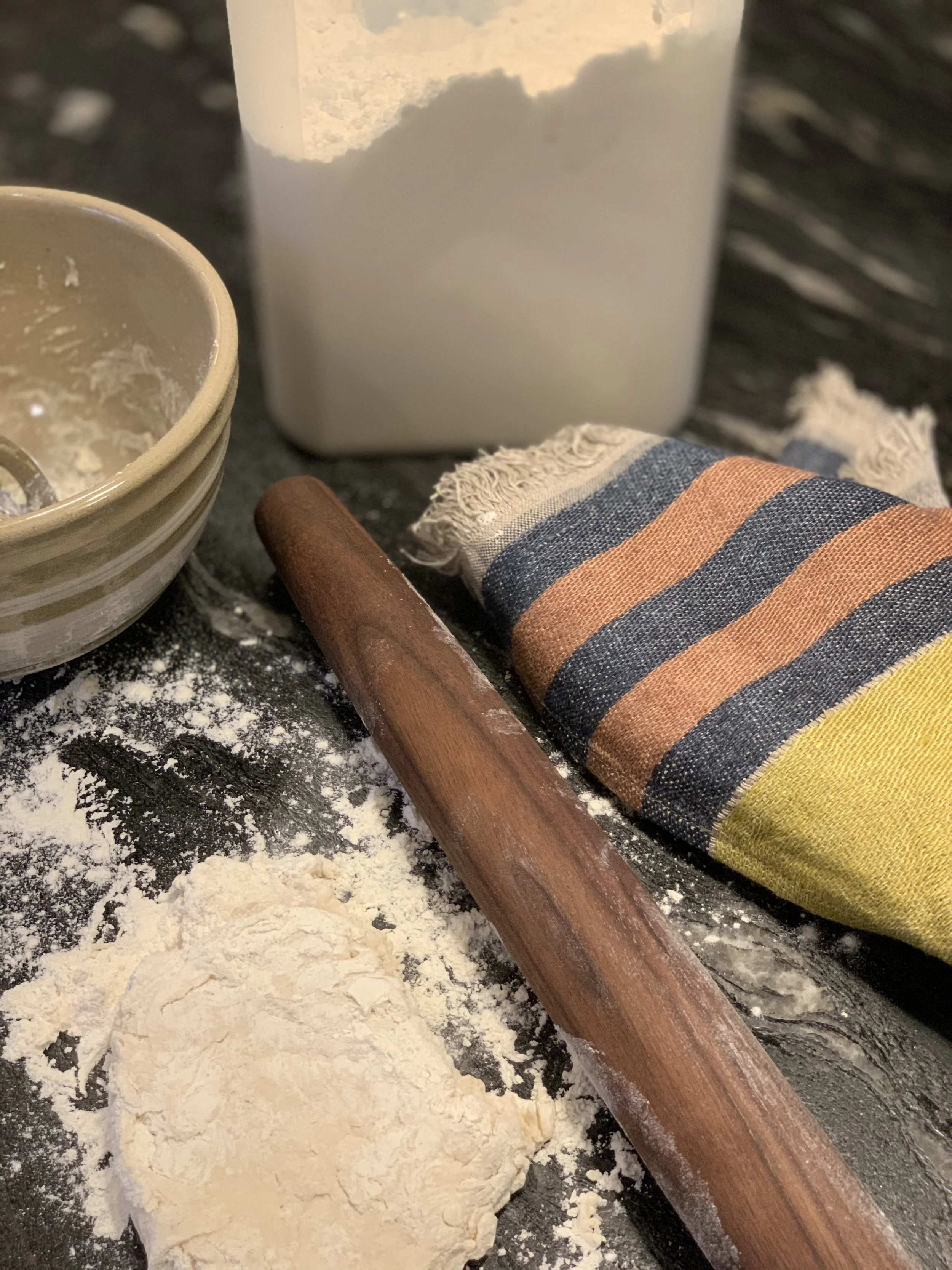 French rolling pin, Libeco linen, and a handmade yellowware bowl with flour on a kitchen counter, from MERZE Lifestyle.