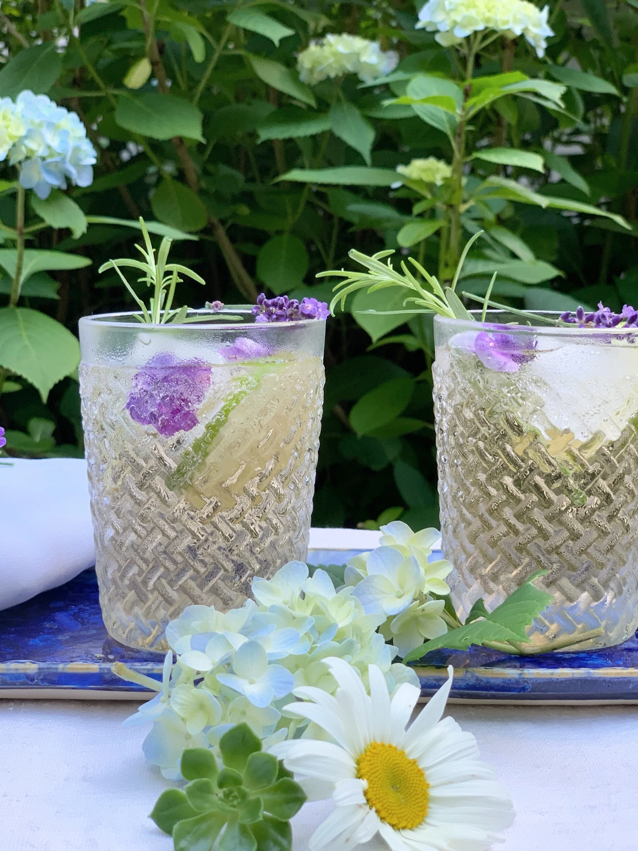 Side view of a garden drink garnished with lavender and violas with hydrangeas softly blurred in the background.